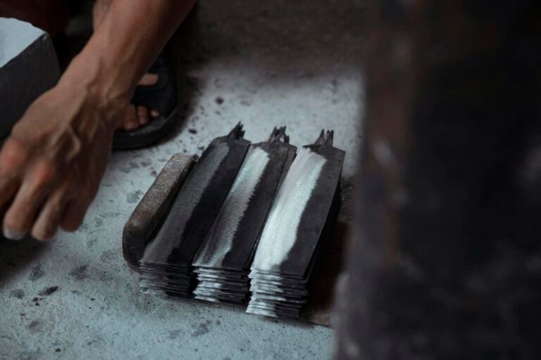 Close-up of knife blades being prepared by a craftsman, showcasing traditional metalwork.